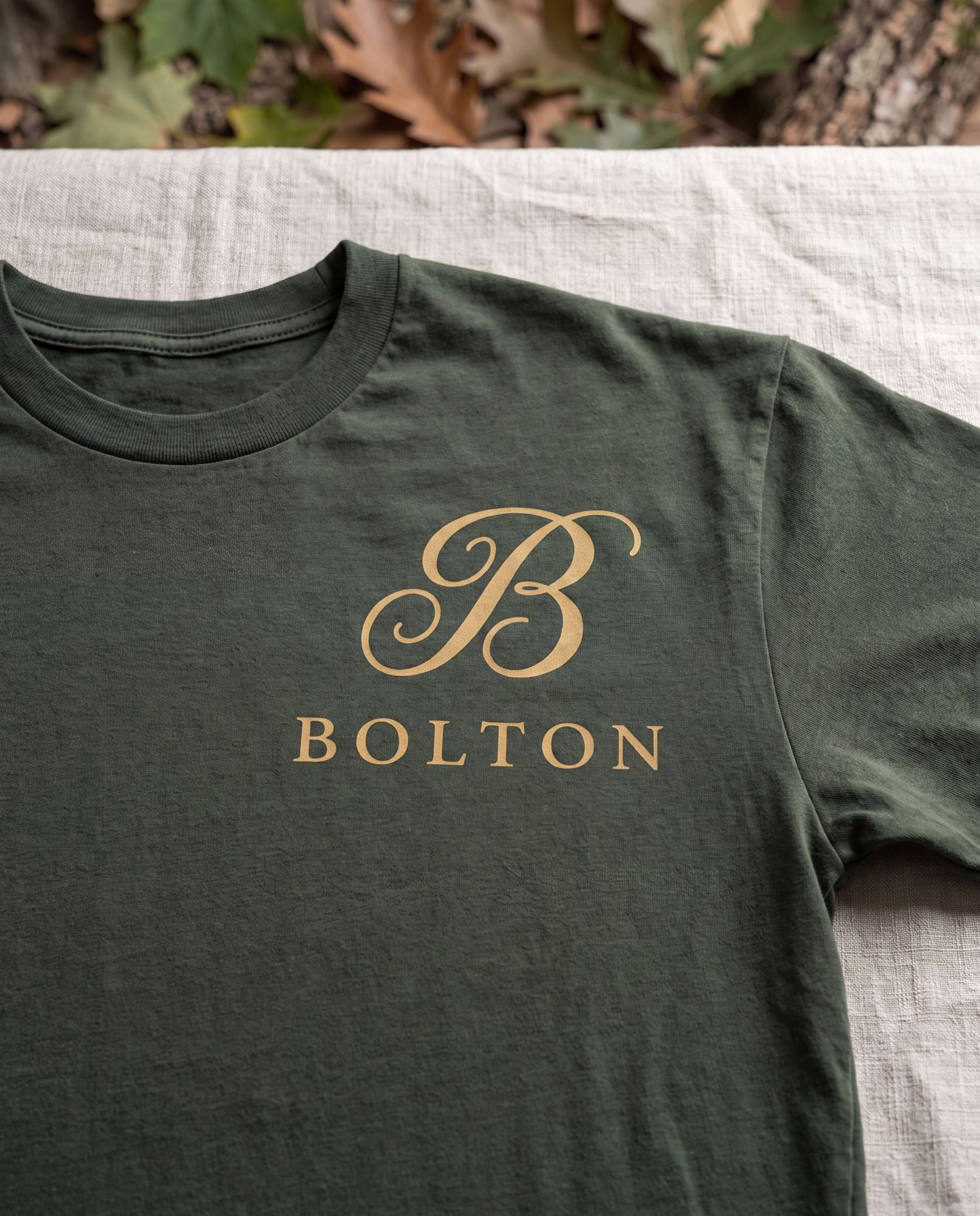 A moss t-shirt with the B and BOLTON printed in honey